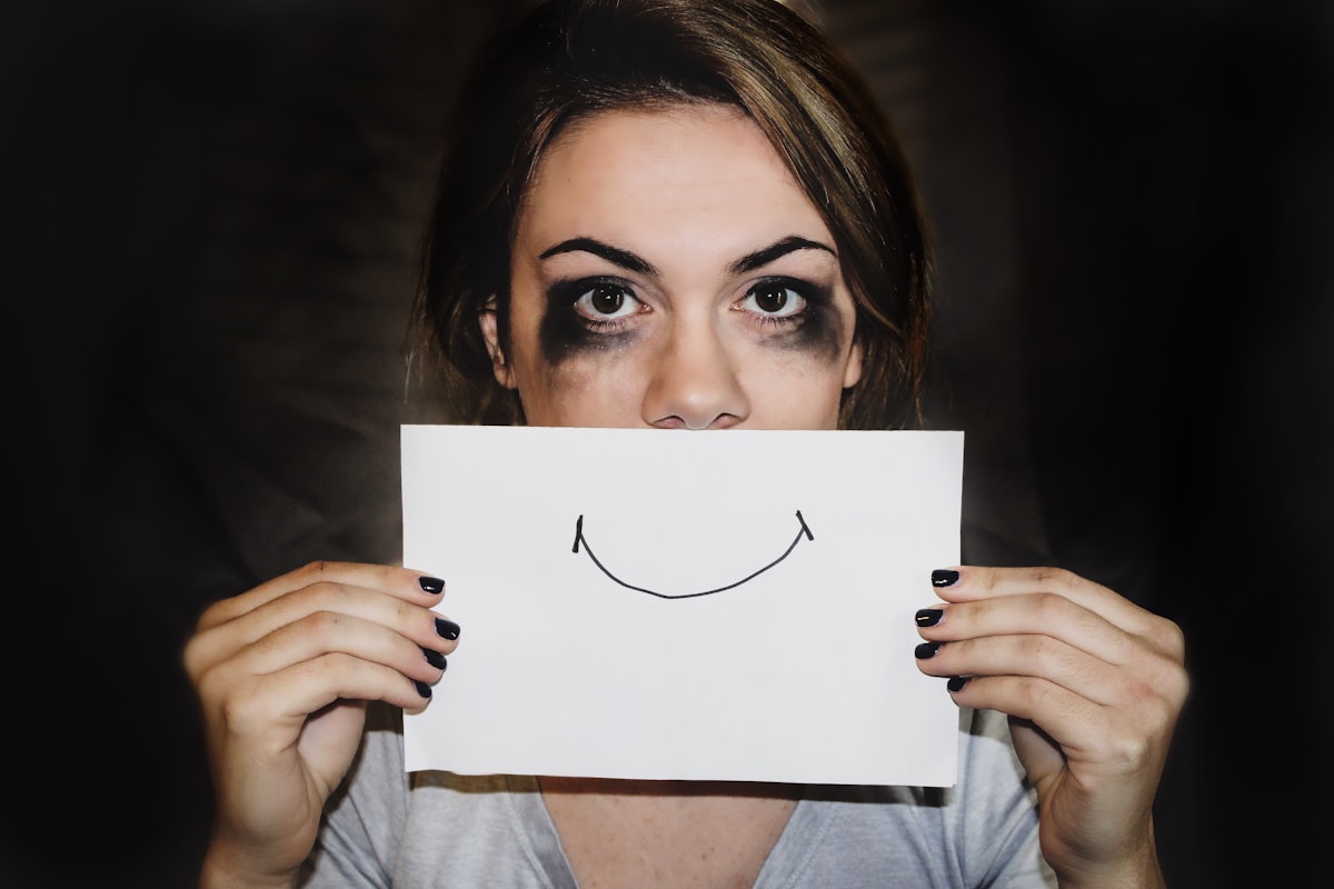 A woman holding a smiling paper in front of her face, representing shame, secrecy and hidden overwhelm behind addictive behaviours